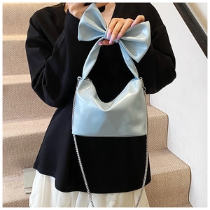 Detail of light blue patent leather handbag with oversized bow handle and silver chain
