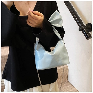 Close-up of metallic light blue bow handbag with silver chain strap on a model