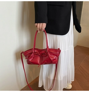 Gros plan d'un sac seau en cuir rouge avec nœud porté sur un blazer noir