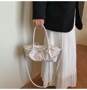 Detail of beige pleated leather tote bag featuring a decorative bow and versatile straps