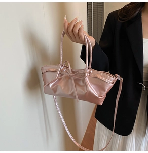 Detail of light pink metallic bag with bow and textured folds held by a model