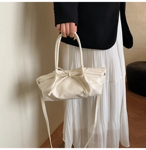 Detail of a creamy white leather handbag with elegant bow decoration and slim handles
