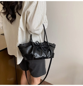 Detail of black pleated PU leather tote bag with elegant bow tie strap on female model