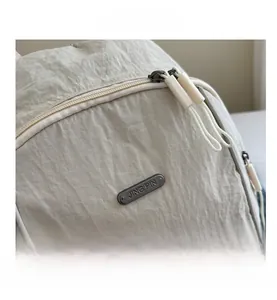Close-up of dual zippers and metal JING PIN logo on the beige nylon backpack