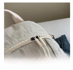 Close-up of smooth dual zippers with woven pull cords on cream nylon backpack