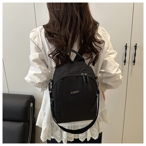 Detail of a black nylon backpack featuring a JING PIN metal logo and dual zippers