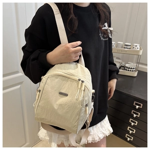 Dettaglio di uno zaino in nylon beige con spallacci regolabili e tasche multiple con zip