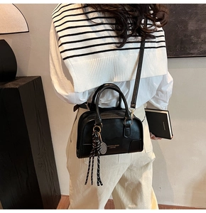 Detail of a chic black Boston bag with fashion branding and woven rope charm accessory