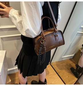 Detail of coffee brown leather boston bag with gold lettering and woven charm accessory
