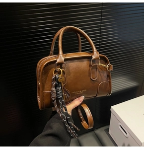 Detail of a brown leather boston bag with twin handles and tennis racket charm accessory