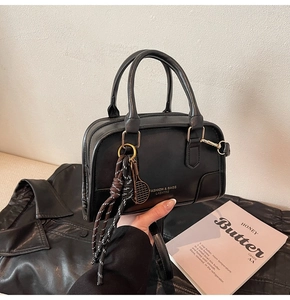 Close-up of black leather Boston bag with tennis racket charm and woven rope detail