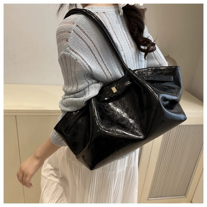 Details einer schwarzen glänzenden Schultertasche mit Falten und Gold-Schnalle