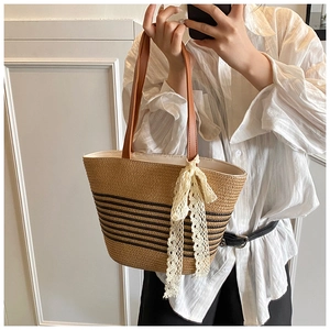 Detail of woven straw tote bag with black stripes and brown leather handle