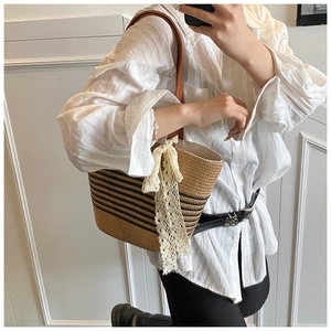 Detail of striped woven tote bag featuring brown leather strap and white lace bow accessory