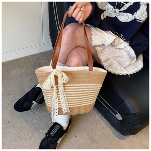 Detail of woven straw bucket bag with leather handles and white lace bow decoration