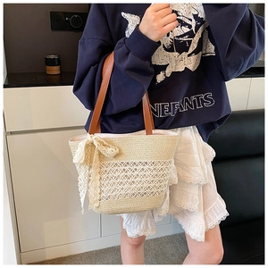 Close-up of woven straw tote bag with delicate lace bow and brown leather strap detail