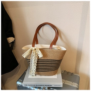 Detail view of woven straw tote bag with black stripes and elegant white lace bow