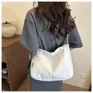 Rear view of a minimalist white half-moon canvas shoulder bag worn by a model