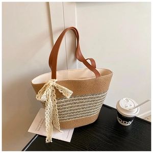Detailed shot of a woven straw bucket bag featuring a lace bow and brown leather handles