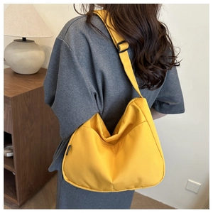 Model wearing a yellow nylon hobo shoulder bag with adjustable strap in home setting