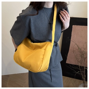 Detailed view of the bright yellow nylon messenger bag worn by a model in gray outfit