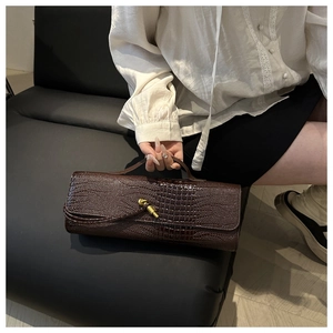 Close-up of a dark brown crocodile pattern leather handbag with a golden metal twist lock