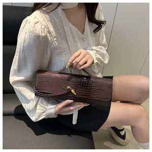 Detail of dark brown crocodile embossed leather bag with brass twist lock and handle