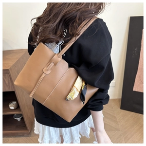 Brown tote bag with white contrast stitching and silk scarf accessory on shoulder