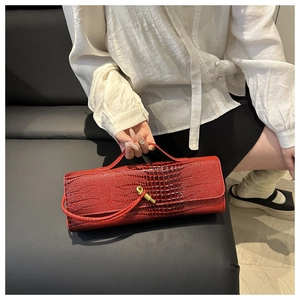 Detail of red crocodile pattern handbag with gold clasp held by a model in casual setting