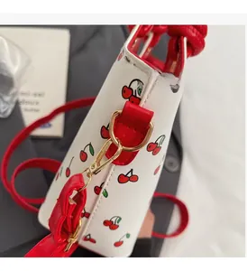 Détail du sac à imprimé cerise blanc avec garniture en cuir rouge et crochets dorés