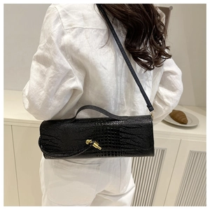 Black crocodile embossed crossbody bag with gold buckle worn on white linen outfit