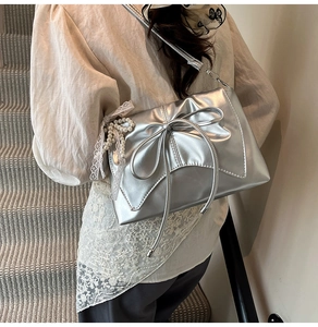Detail of silver metallic tote bag with large bow and pearl lace pendant accessory