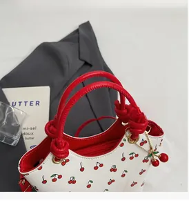 Détail de l'imprimé cerise sur cuir blanc avec poignées rouges et breloque cerise