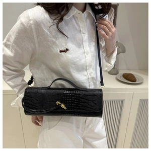 Detail of black cylindrical crossbody bag with crocodile texture and gold knot lock