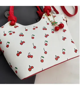 Détail d'un sac blanc à imprimé cerise avec poignée rouge et breloque cerise
