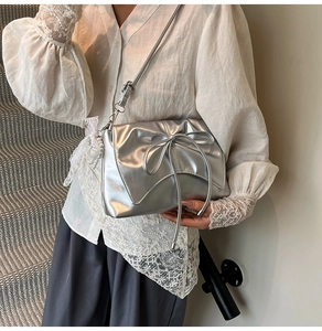 Détail du sac bandoulière argenté avec nœud et pendentif en perles de dentelle