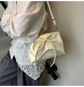 Detail shot of a creamy white crossbody bag featuring a chic bow and soft leather texture