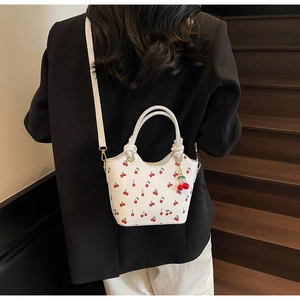 Détail du sac seau blanc à motif cerise avec bandoulière porté sur un blazer noir