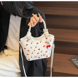 Détail d'un sac cabas blanc à imprimé cerise et breloque cerise porté par un modèle