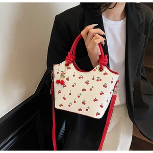 Détail du sac cabas blanc avec imprimé cerises, anses tressées rouges et breloque