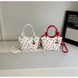 Détail de sacs cabas à imprimé cerise avec poignées rouges et breloques cerises 3D
