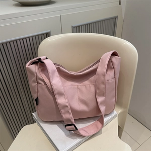 Pink waterproof nylon shoulder bag for women with wide strap on a white chair