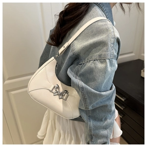 Détail d'un sac demi-lune blanc crème avec un fermoir papillon argenté porté à l'épaule