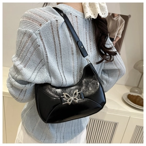 Détail d'un sac hobo noir brillant avec une boucle métallique en forme de papillon argenté