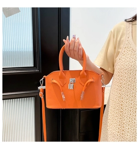 Detail van een feloranje schelptas met zilveren slot en leertextuur met lychee-korrel