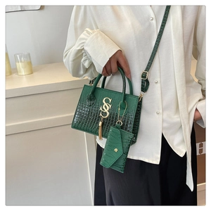 Detail of green crocodile embossed handbag with gold S-buckle and tassel charms