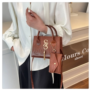 Detail of dark brown crocodile embossed tote bag with gold S logo and fringe charm