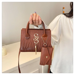 Detail of caramel brown crocodile embossed handbag with gold S metal tassel charm