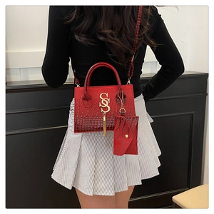 Detail of red croc-embossed handbag with metal S-logo, fringe, and matching mini pouch