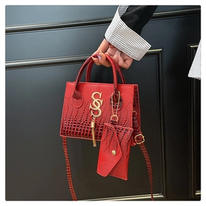 Detail of red crocodile pattern handbag with gold S logo, tassel, and matching coin purse